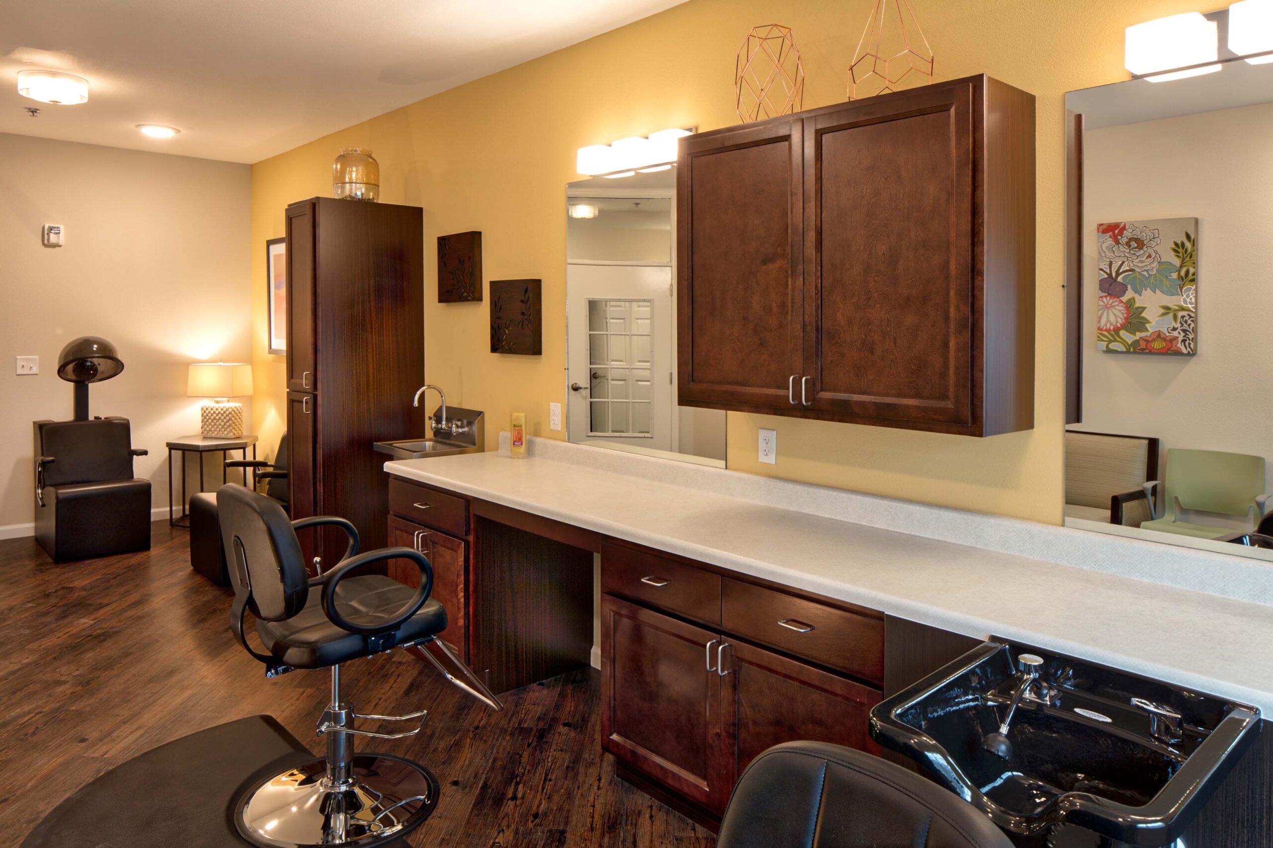 Jim Wilson3D3A5773RT1A - Twin Rivers A beauty salon with dark brown cabinets and black chairs at Twin Rivers, an assisted living and memory care community near Garland, TX.
