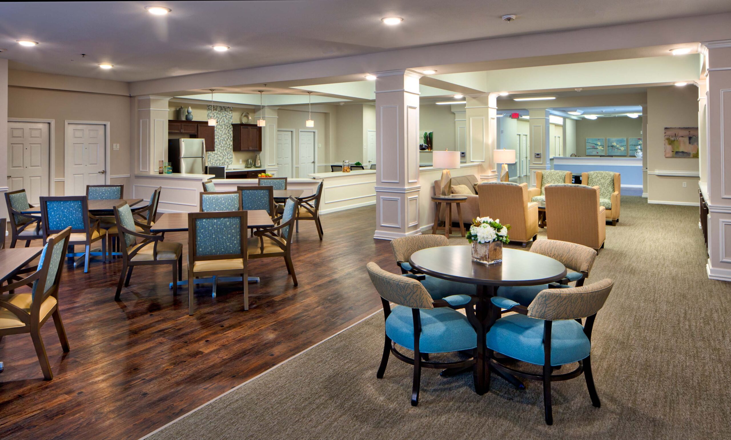 Jim Wilson3D3A5867RT1ACAB - Twin Rivers A sitting area with tables, blue and mustard cushioned chairs, and flower bouquets on each table at Twin Rivers, an assisted living and memory care community near Dallas.