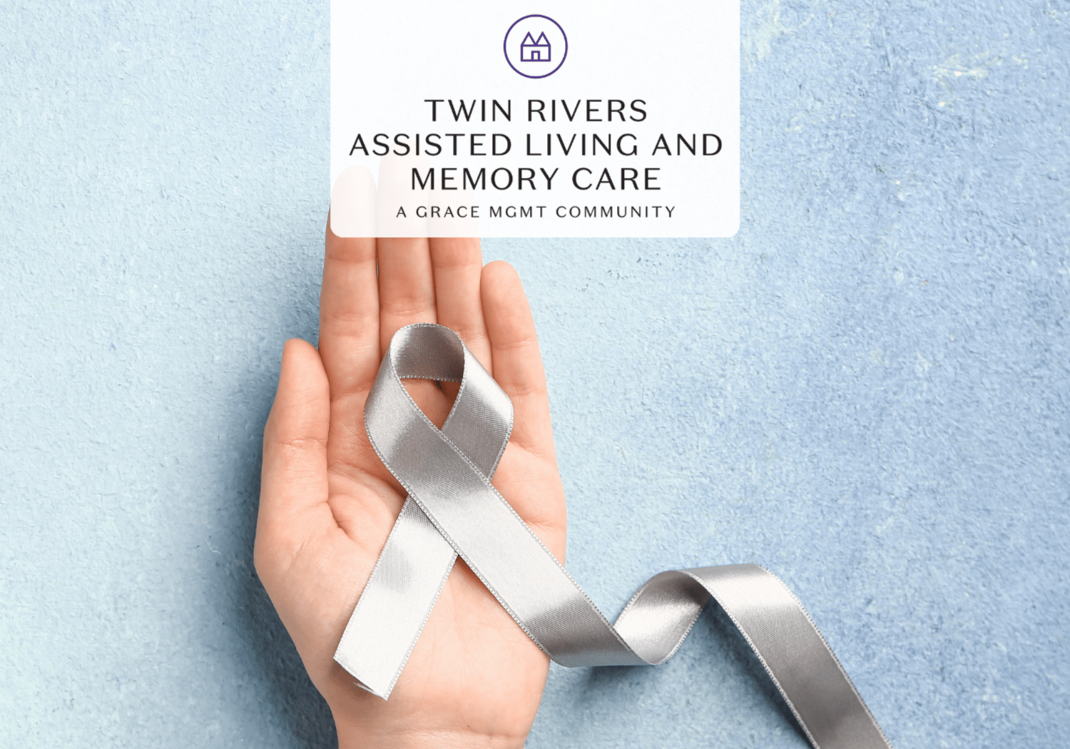Hand holding a silver awareness ribbon over a blue background with a card that reads 'Twin Rivers Assisted Living and Memory Care'