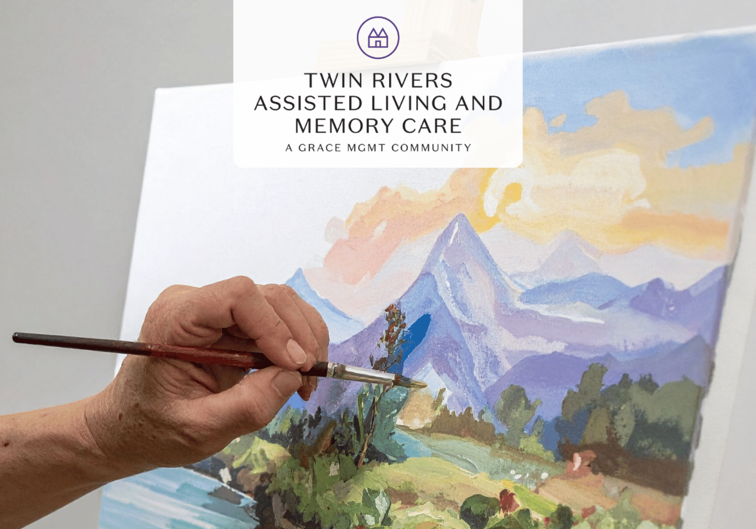 Close-up of an elderly hand holding a paintbrush, painting a colorful mountain landscape on canvas with a Twin Rivers Assisted Living and Memory Care logo overlay.